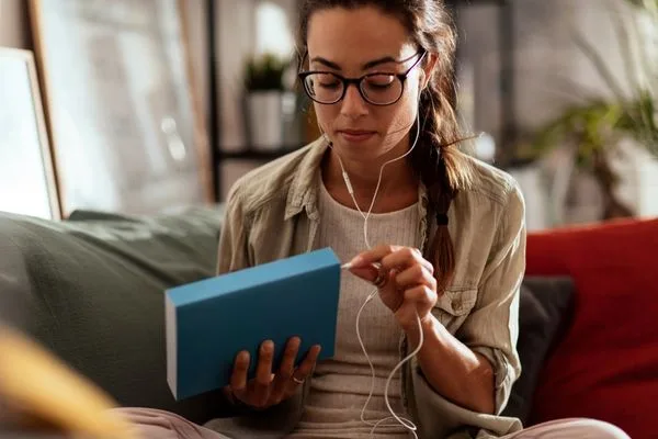 Is Audible worth it? A white woman with dark hair and glasses wearing headphones and plugging them into a book
